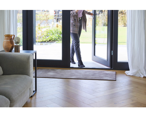 Eingangsbereich mit Fußmatte, Holzboden und einer Frau, die durch eine Tür geht