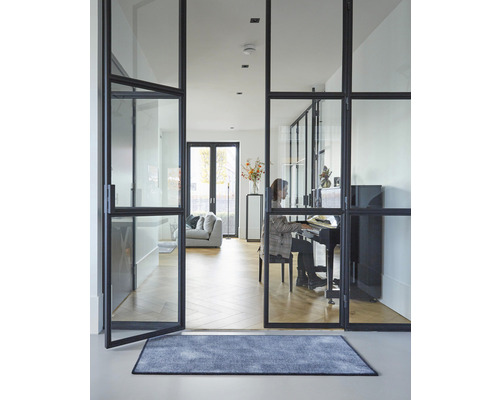 Innenaufnahme eines Wohnraums mit Glastüren, Teppich und einer Person am Klavier.