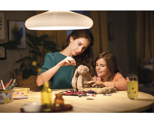 Mutter und Tochter sitzen an einem Tisch unter einer Lampe und flicken ein Stofftier.
