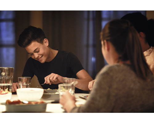 Personen sitzen am Esstisch und essen Speisen aus Schüsseln und Tellern.