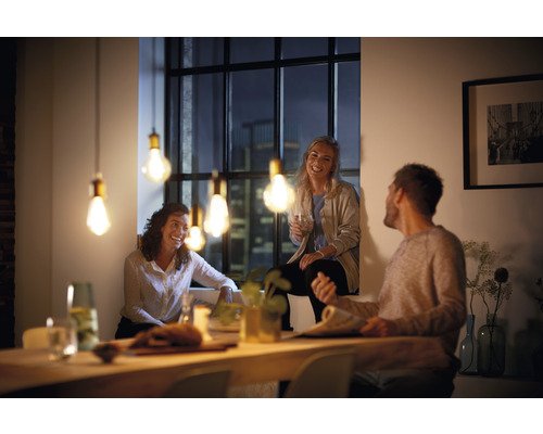 Szene mit drei Personen an einem Tisch, beleuchtet durch Pendelleuchten