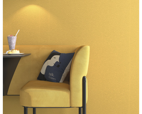 Gelbe Wand mit Textiltapete, Sessel mit Kissen und Getränk auf kleinem Tisch