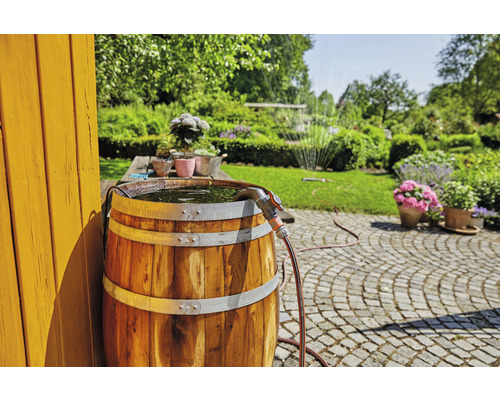 Holz Regentonne mit Wasser befüllt und einem Gartenschlauch im sonnigen Garten.