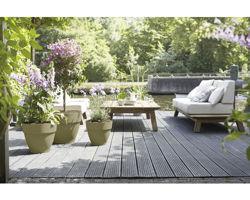 Gartenszene mit Pflanzkübeln, Holzboden, Couch und Tisch am Wasser