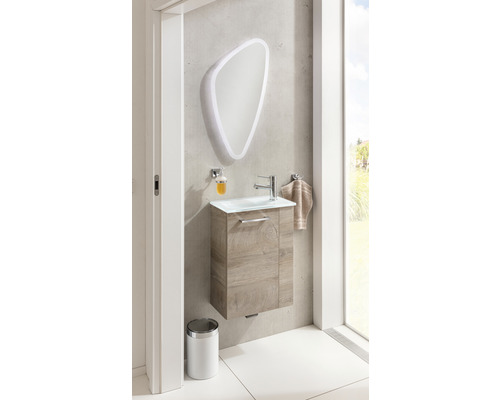 Badezimmer mit Waschbeckenunterschrank, Spiegel mit Beleuchtung, Seifenspender, Handtuch und Abfalleimer.