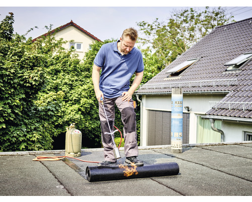 Handwerker verschweißt Bitumenbahn auf einem Flachdach mit einem Schweißbrenner