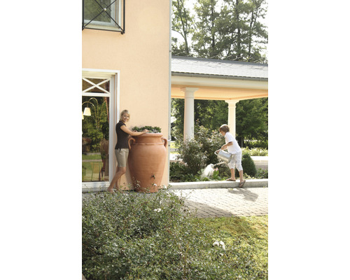 Frau an Regentonne in Amphorenform und Kind beim Gießen von Pflanzen im Garten