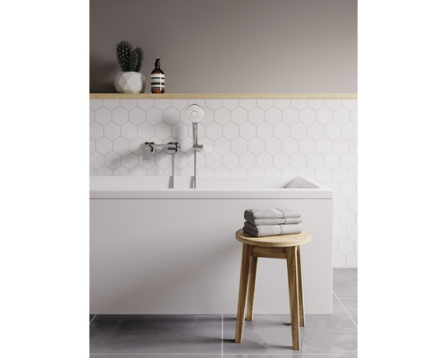 Helles Badezimmer mit Badewanne, Handbrause, Handtüchern und Holzhocker.