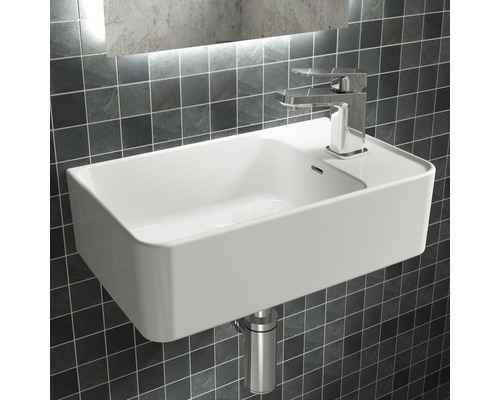 Weißes Waschbecken mit Armatur und Siphon vor einer gefliesten Wand