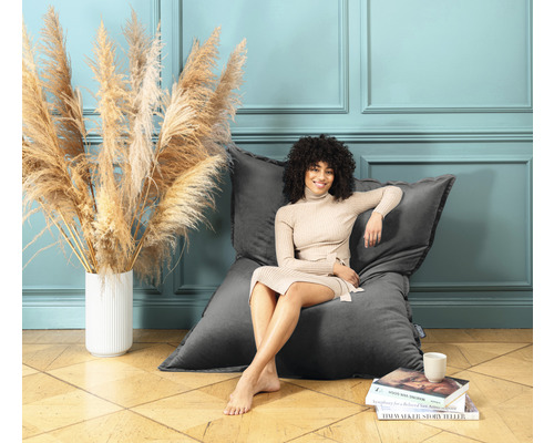 Frau sitzt entspannt auf einem grauen Sitzsack in einem Zimmer mit dekorativer Blumenvase