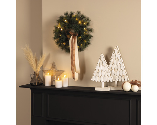Dekoratives Arrangement mit Kranz, LED-Kerzen und Deko-Bäumen auf einem Kaminsims
