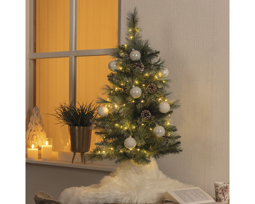 Dekorierter künstlicher Weihnachtsbaum mit Beleuchtung, Kugeln und Tannenzapfen in Wohnraum