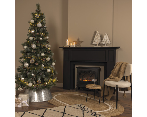 Dekorierter Weihnachtsbaum neben Kamin und Stuhl in einem Wohnzimmer.