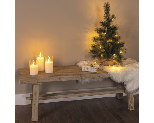 Dekorative Szene mit Bank, Kerzen, kleinem Weihnachtsbaum, Geschenk und Fellteppich für eine festliche Atmosphäre