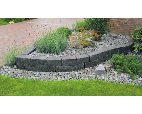 Gartenanlage mit einer Mauer aus grauen Betonsteinen, umgeben von Pflanzen und Steinen.