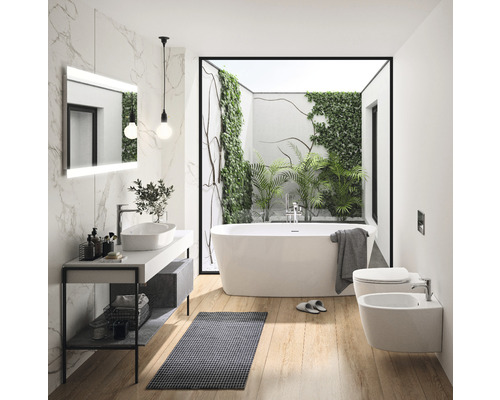 Helles Badezimmer mit Badewanne, Waschtisch, Spiegel und Bidet vor einem Fenster mit Pflanzen