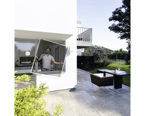 Mann montiert Insektenschutzgitter am Fenster eines modernen Hauses mit Terrasse