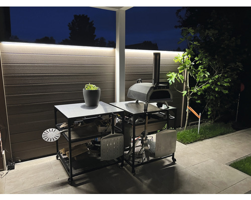 Außenbereich mit Pizzaofen auf einem Servierwagen mit Regalen für Holz und Zubehör.