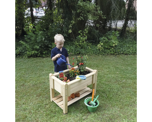 Kind gießt Pflanzen in einem Hochbeet aus Holz im Garten.