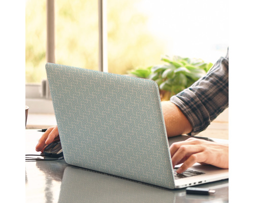 Laptop mit Musterbezug auf einem Schreibtisch, Person tippt auf der Tastatur.