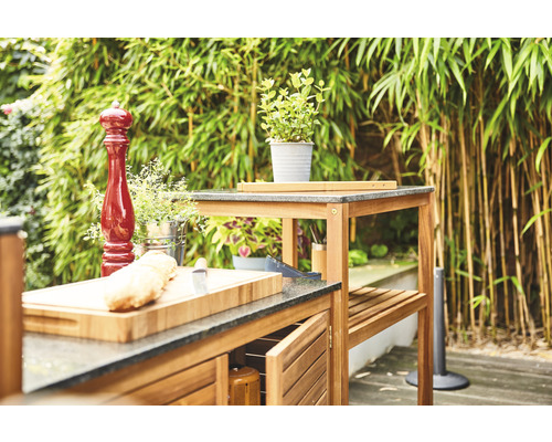 Outdoor-Küche mit Arbeitsplatten, Schränken und Regalen vor natürlichem Hintergrund.