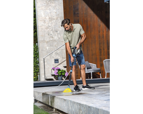 Mann reinigt mit einer Bürste und Wasserschlauch eine Terrasse.