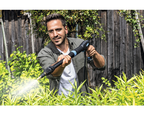 Mann benutzt Hochdruckreiniger im Garten zur Reinigung von Pflanzen