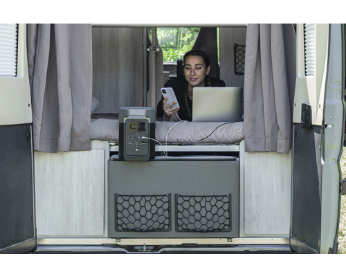 Szene im Van mit tragbarer Powerstation, Frau nutzt Handy und Laptop