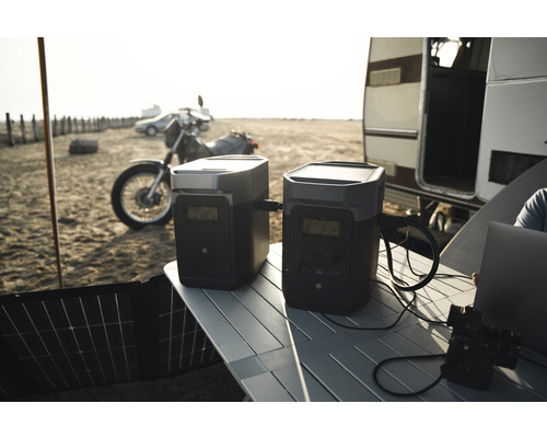 Zwei tragbare Kraftwerke von Ecoflow auf einem Tisch im Freien, mit einem Motorrad und einem Wohnwagen im Hintergrund.