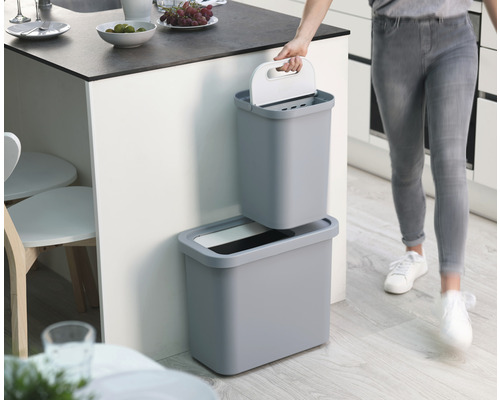 Zweiteiliger, grauer Wertstoffsammler im Küchenbereich, mit Frau, die den oberen Behälter hält.