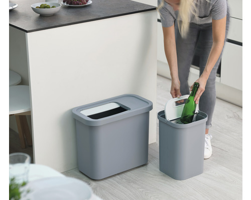 Zwei graue Abfallbehälter in einer Küche, eine Person wirft eine Flasche hinein.