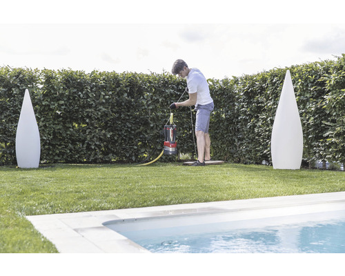Ein Mann bedient eine Schmutzwasserpumpe in einem Garten nahe einem Pool, flankiert von zwei Deko-Leuchten.