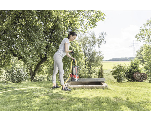 Frau bedient eine Tauchpumpe in einem Betonschacht im Garten.