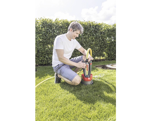 Ein Mann hockt auf einem Rasen und schliesst einen gelben Schlauch an eine Tauchpumpe von Al-Ko an.