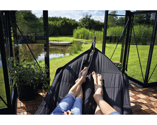 Personen entspannen sich in einer Hängematte in einem Gewächshaus mit Blick auf einen See