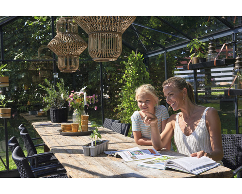 Gewächshaus-Interieur mit Holztisch, Stühlen, Pflanzen und zwei Personen