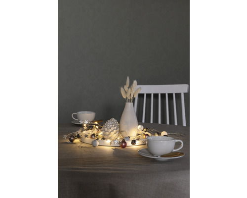 Dekoration mit Lichterkette, Tannenzapfen, Vase und Tassen auf einem Tisch