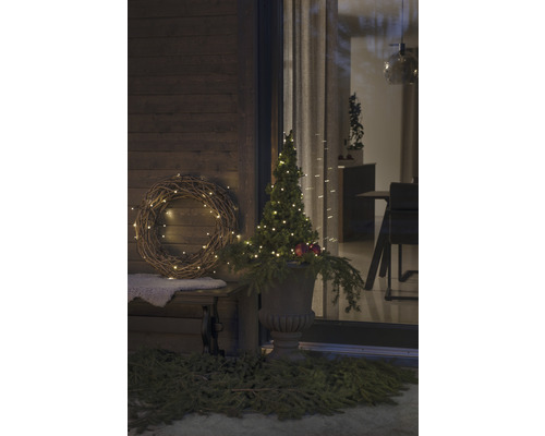 Dekorierte Veranda mit Kranz, beleuchtetem Baum und Pflanzgefäß