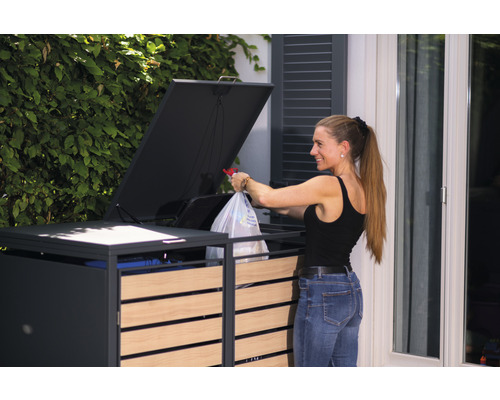 Frau entsorgt Müll in einer Mülltonnenbox mit Holzelementen und Klappdeckel