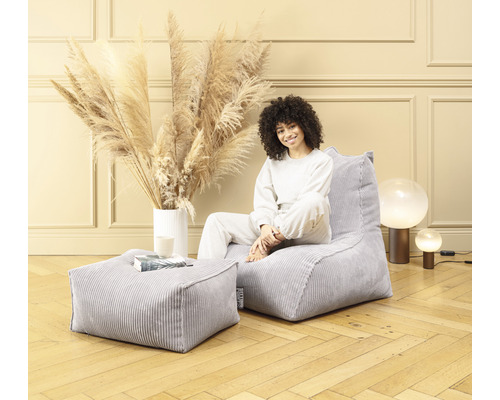 Frau sitzt auf einem grauen Cord-Sitzsack mit passendem Hocker in einem hellen Raum.