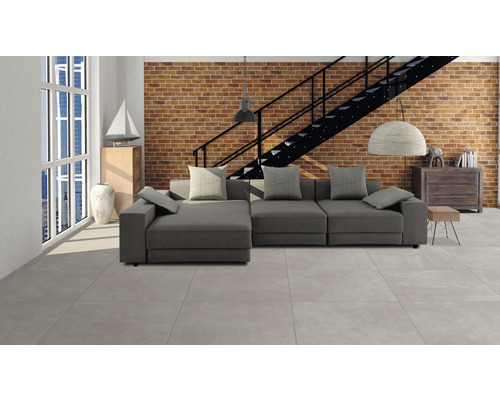 Helles Wohnzimmer mit grauer Couch, Ziegelwand und Treppe.