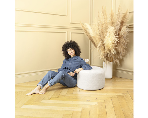 Frau sitzt auf einem runden, weißen Hocker in einem Zimmer mit Holzboden