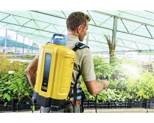 Mann verwendet einen Rückensprüher im Gewächshaus.