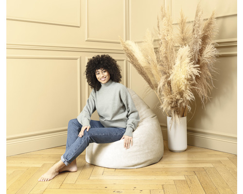 Frau sitzt auf einem hellen Sitzsack in einem Zimmer mit Trockenblumen in einer Vase.