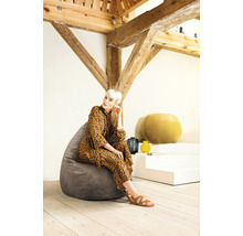 Frau sitzt auf einem grauen Sitzsack in einem hellen Raum mit Holzbalken.