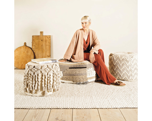 Wohnszene mit Frau, die auf einem Pouf sitzt, weitere Poufs und Holzteller im Hintergrund