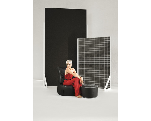 Frau sitzt auf einem schwarzen Sessel mit Fußhocker vor dekorativen Paneelen