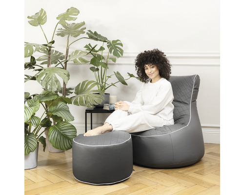 Frau sitzt auf einem grauen Sitzsack mit Fußhocker im Wohnzimmer.