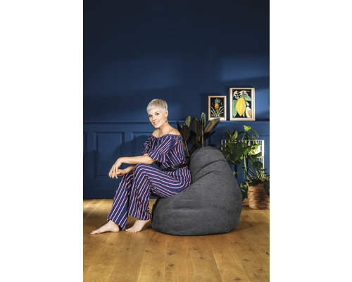 Frau sitzt auf einem grauen Sitzsack in einem Wohnraum mit Pflanzen und Dekoration