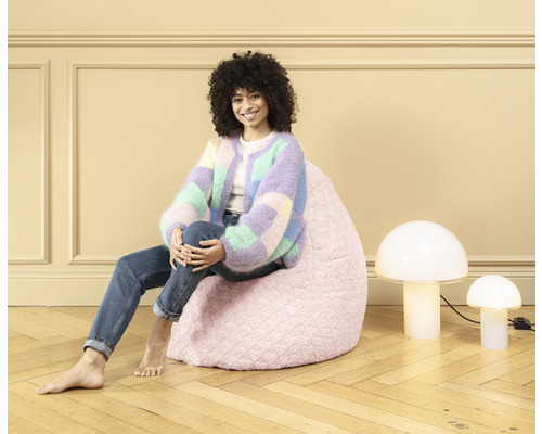 Eine Frau sitzt auf einem rosa Sitzsack neben zwei Pilzlampen.